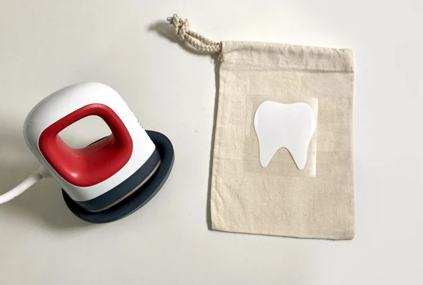 Small drawstring tooth fairy bag with white tooth design beside a Cricut heat press