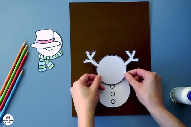 Hands pasting the middle snowman body piece onto a paper snowman craft