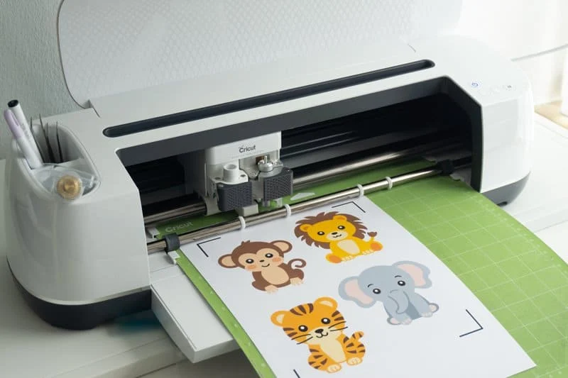Cricut cutting machine with a print and cut animal sticker sheet on a green cutting mat