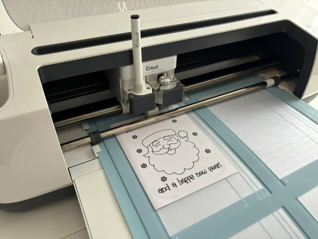 Cricut machine drawing a Santa Christmas card SVG on a blue cutting mat