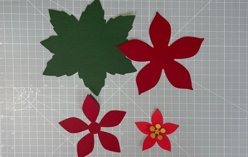 Layered paper poinsettia SVG cut pieces on a gridded craft mat