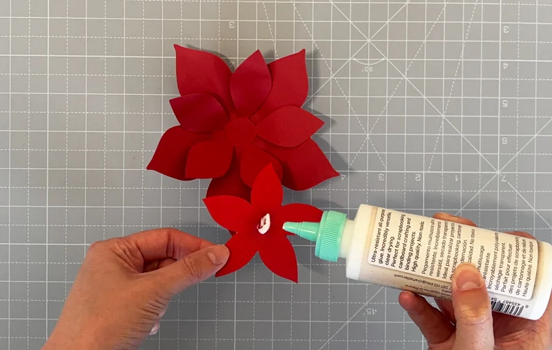 Applying glue to a red paper poinsettia layer on a cutting mat