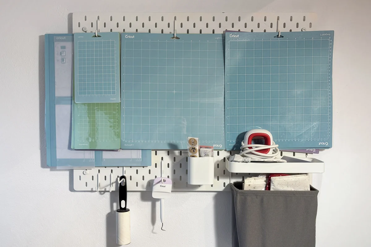 Pegboard craft room organization with Cricut mats, tools, lint roller, and heat press accessories
