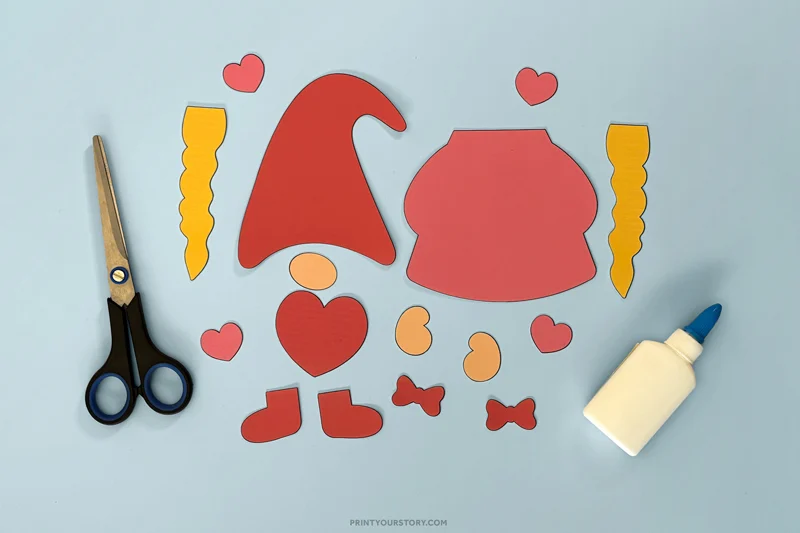 Cut paper pieces for a Valentine gnome craft laid out with scissors and glue