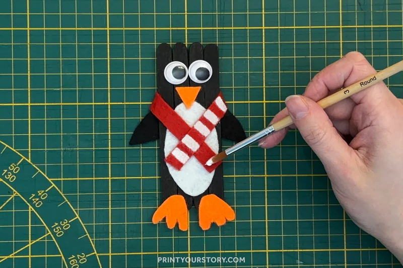 Painting red stripes on a penguin popsicle stick craft with a scarf