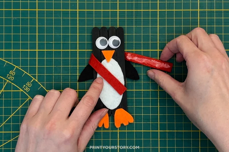 Adding a red scarf to a popsicle stick penguin craft on a cutting mat