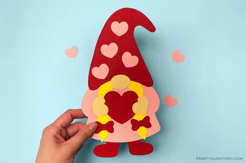 Hand holding a Valentine gnome paper craft with a red heart hat and heart decorations