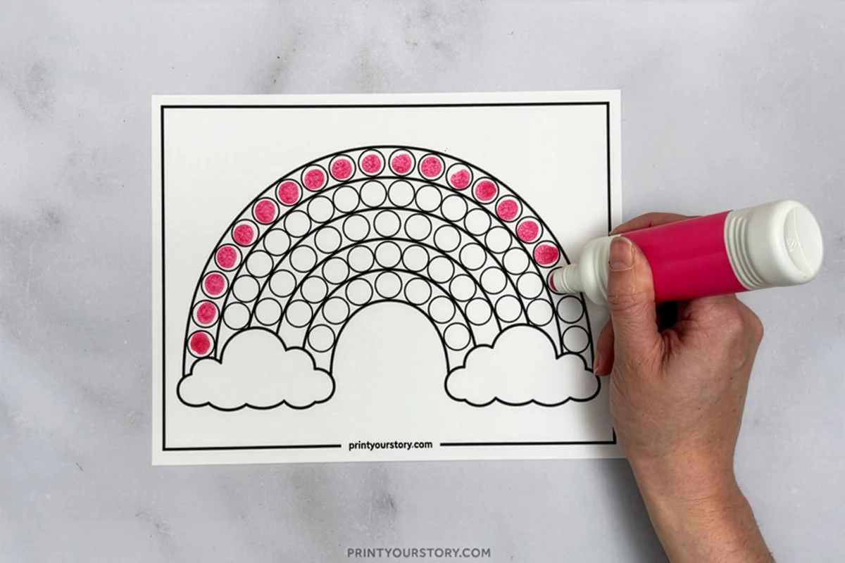 Hand coloring a rainbow dot marker worksheet with a pink marker