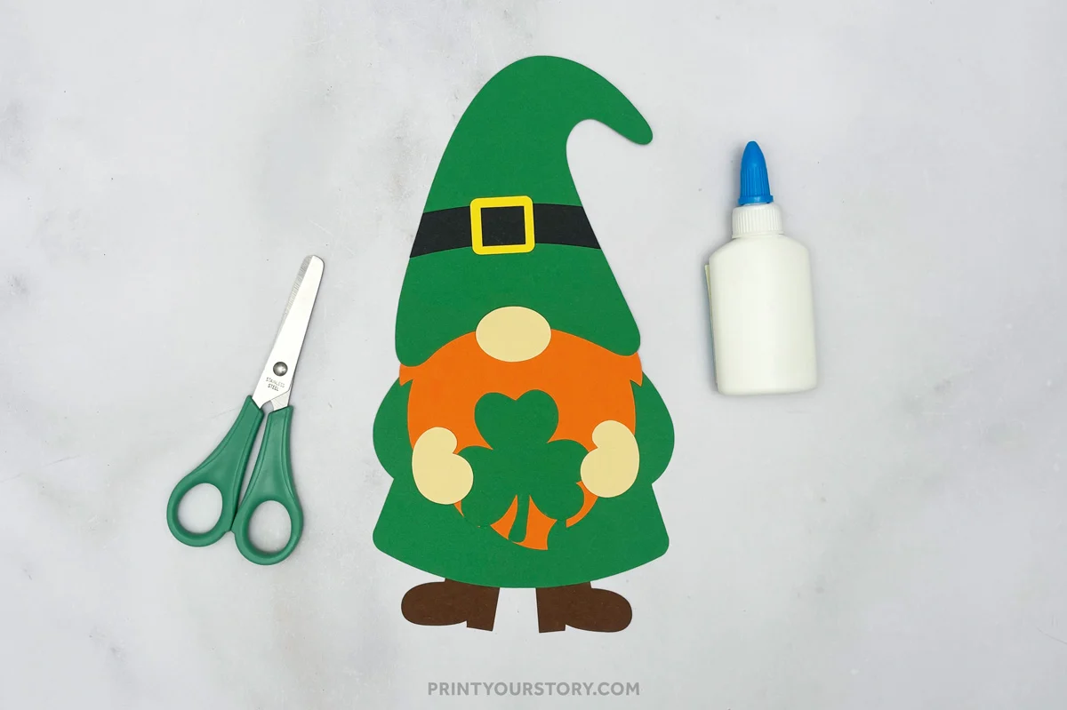 Paper St. Patrick’s Day gnome craft with green hat and shamrock, beside scissors and glue
