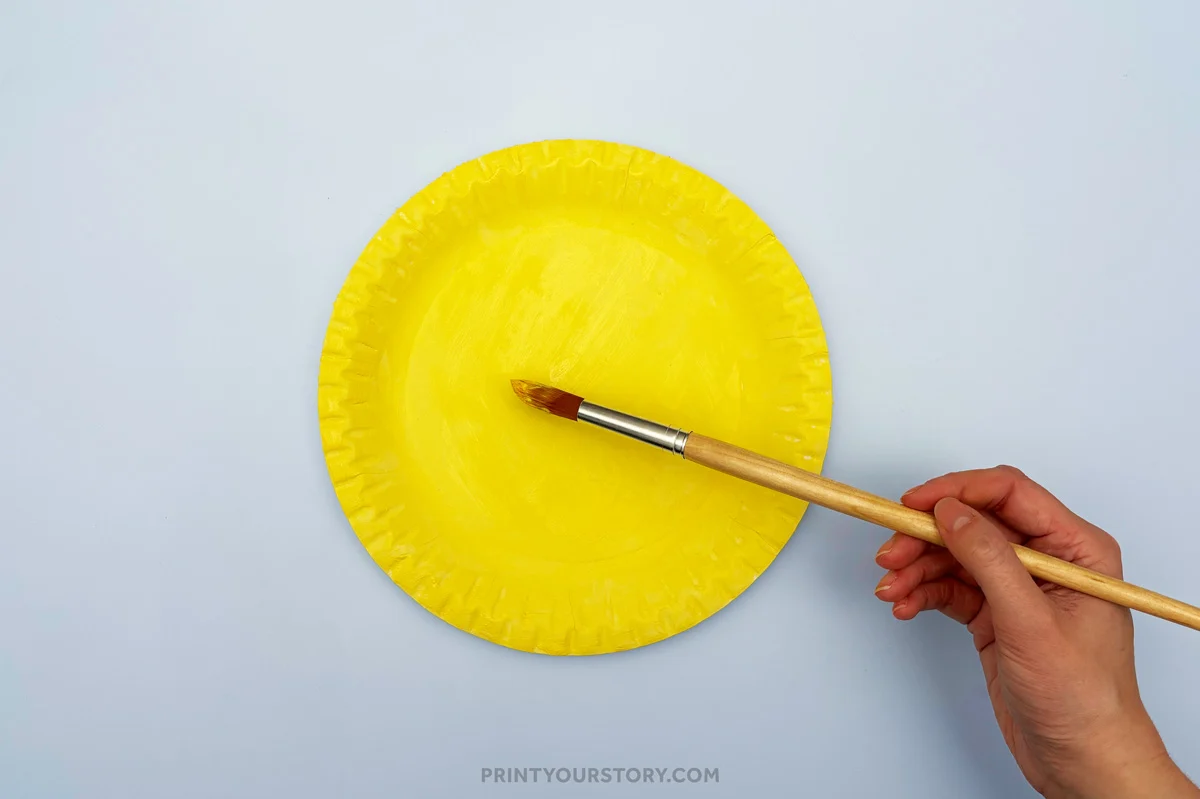 Hand painting a yellow paper plate