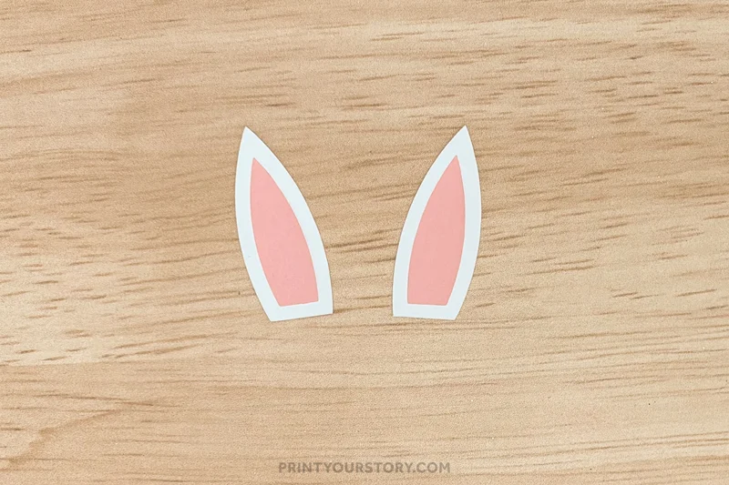 White and pink paper bunny ears cutouts on a wooden surface