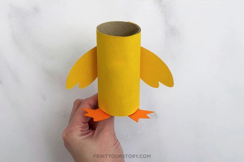 Yellow toilet paper roll chick craft with paper wings and orange feet held in one hand