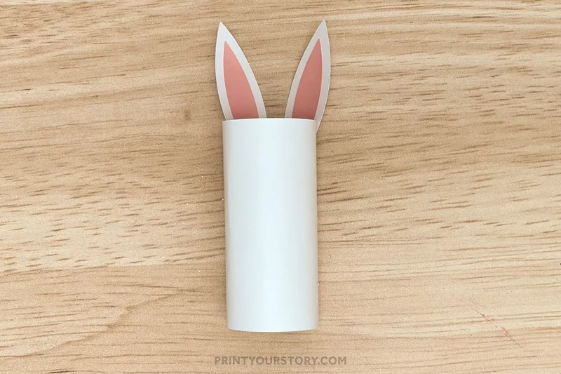 Toilet paper roll bunny craft with paper ears attached on a wooden surface