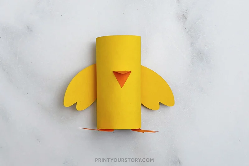Yellow toilet paper roll chick craft with paper wings, beak, and feet on a gray surface