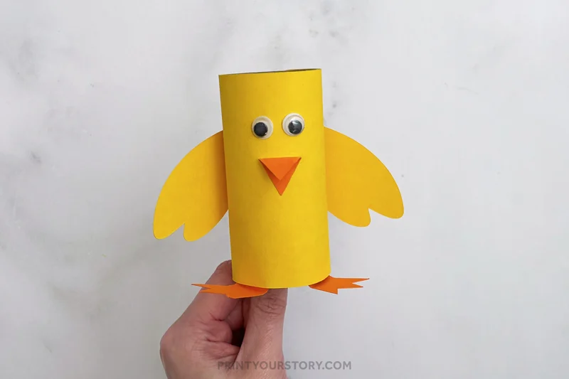 Yellow toilet paper roll chick craft with googly eyes, orange beak, wings, and feet held by hand