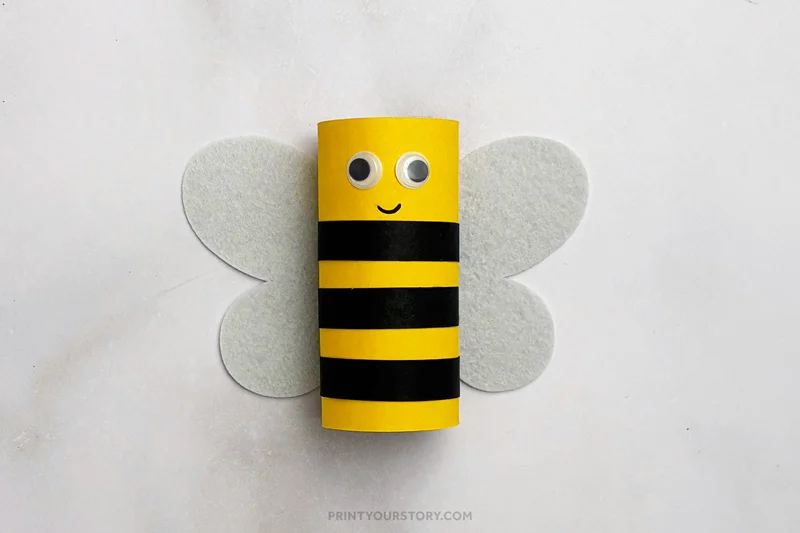 Finished toilet paper roll bee craft with yellow body, black stripes, googly eyes, and white wings