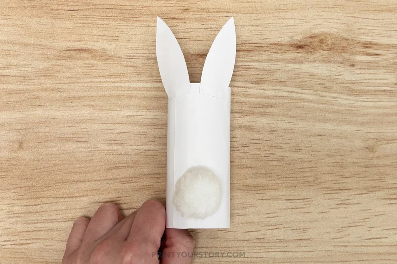 Toilet paper roll bunny craft with white paper ears and a cotton ball tail on a wooden table