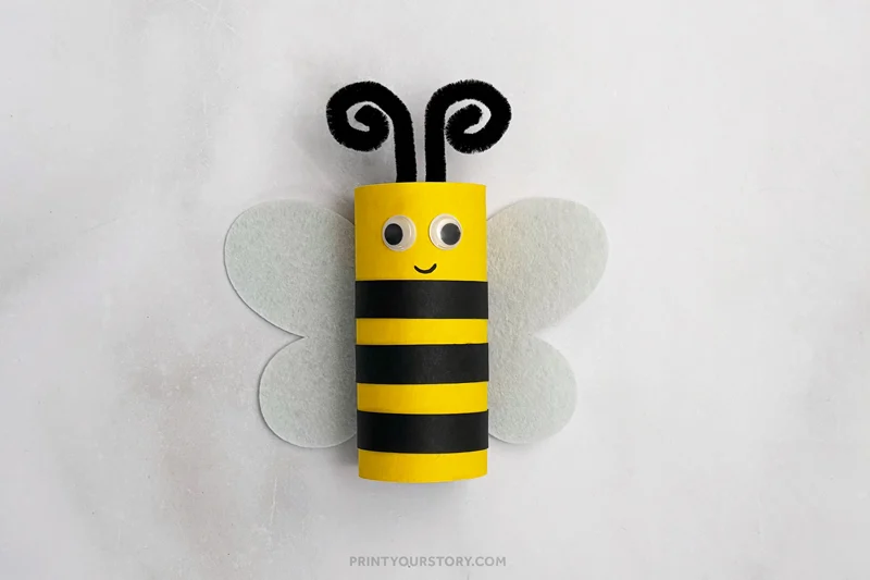 Finished bee toilet paper roll craft with striped body, wings, googly eyes, and pipe cleaner antennae