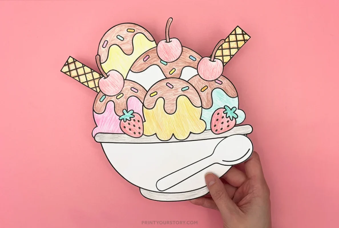 Hand holding colored cut-and-paste paper ice cream sundae craft with scoops, cherries, wafers, strawberries, and spoon