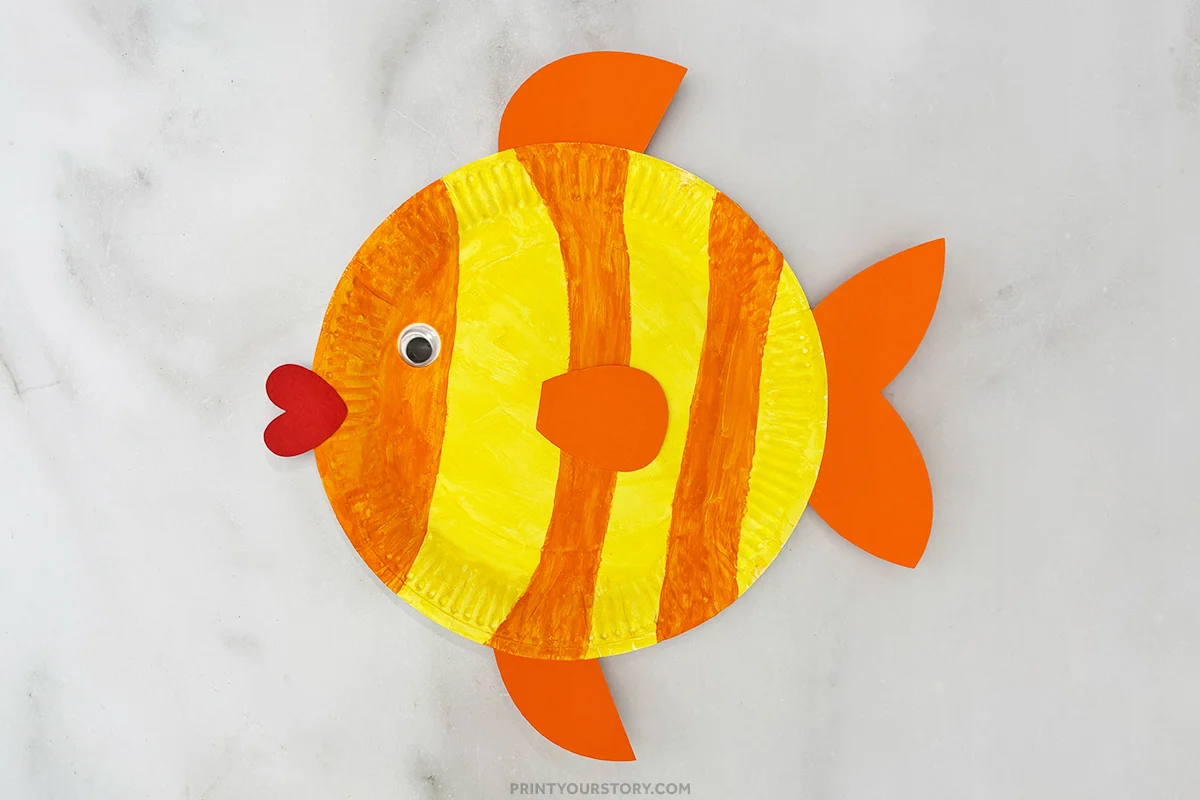 Paper plate fish craft with yellow and orange stripes, fins, googly eye, and red lips
