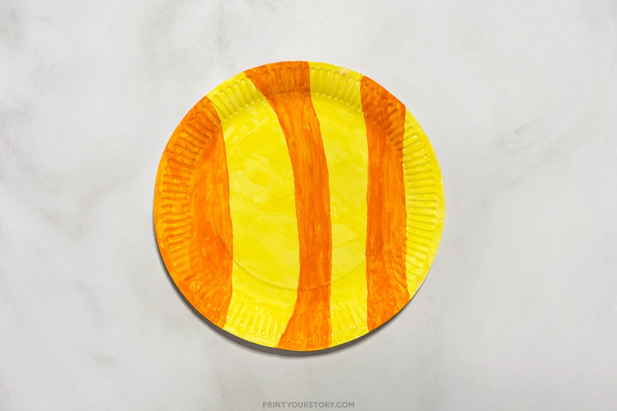 Yellow paper plate painted with orange vertical stripes for a fish craft