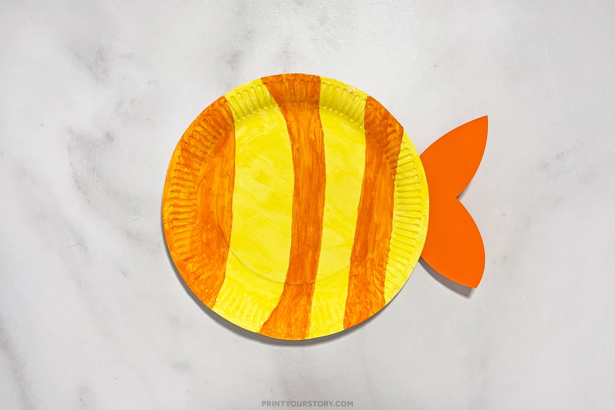 Paper plate painted yellow with orange stripes and orange fins attached for a paper plate fish crafts