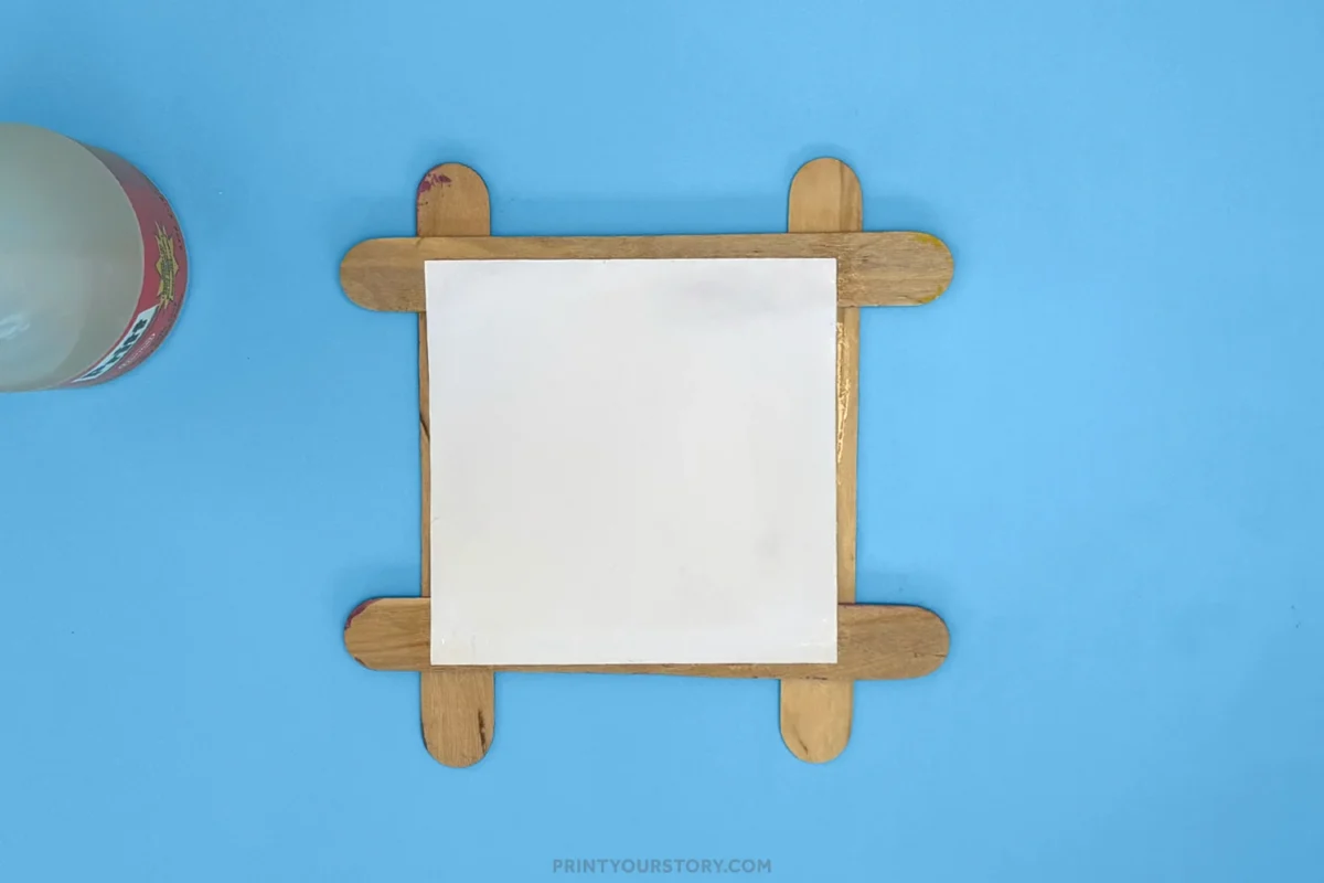 Popsicle stick photo frame with a white paper center on a blue craft surface