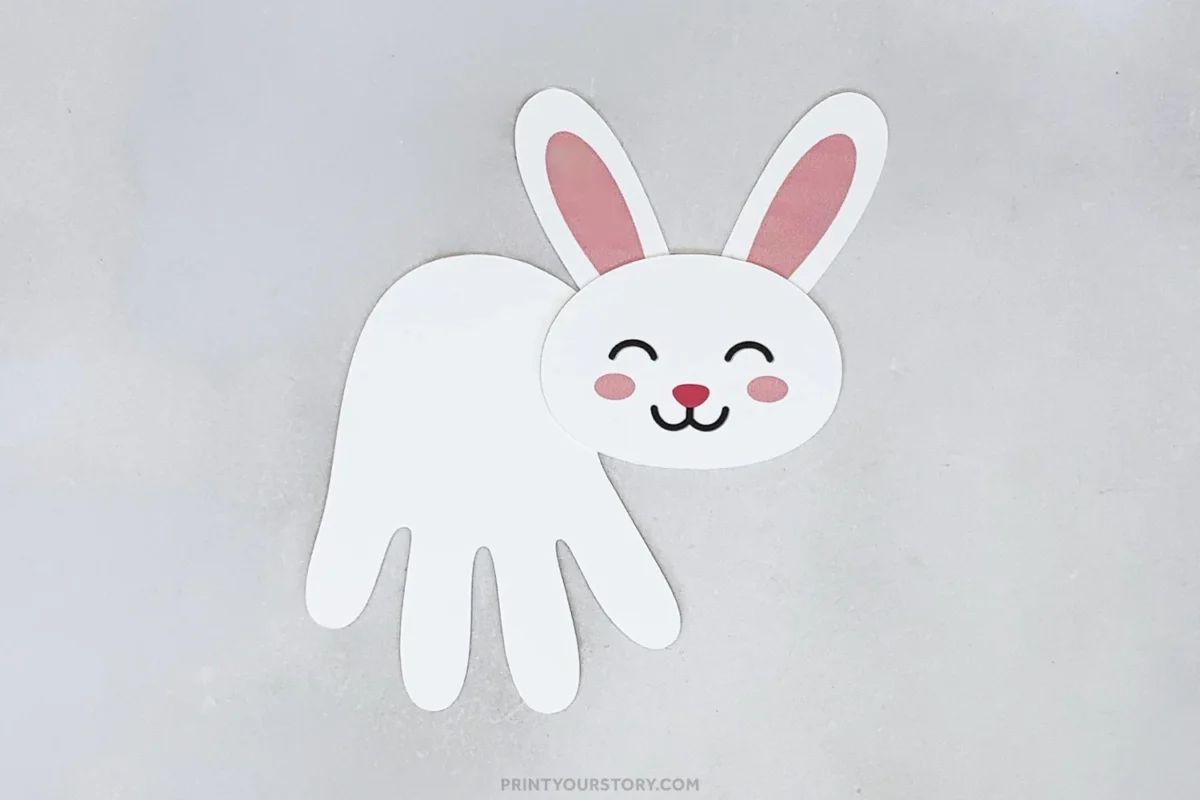 Paper handprint bunny craft with pink ears and a smiling face on a gray background