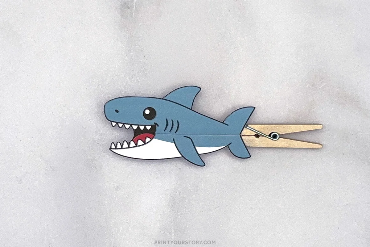 Completed shark clothespin puppet craft with an open mouth attached to a wooden clothespin on a light gray background