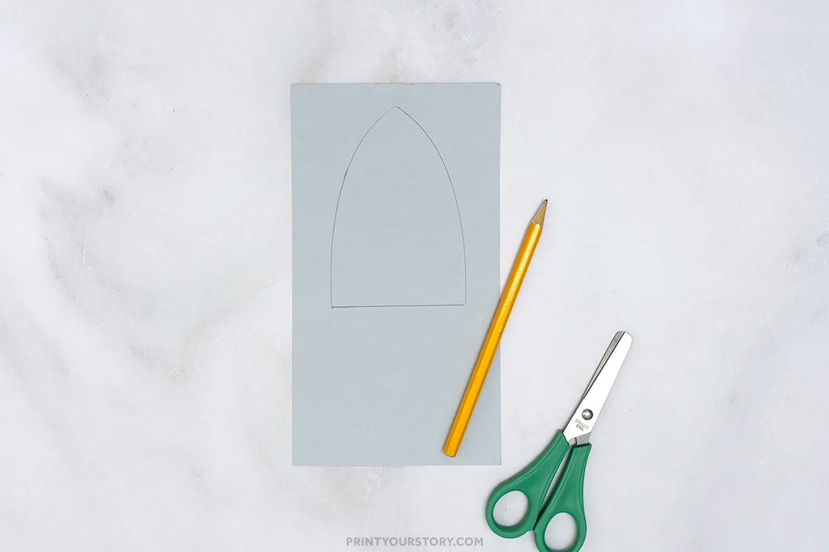 Rocket outline drawn on gray paper with a pencil and scissors beside it
