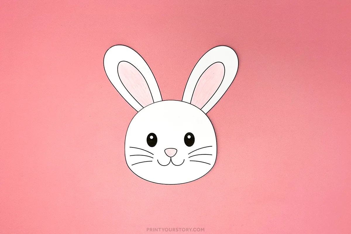 Cut-out paper bunny head with pink ears and nose on a pink background