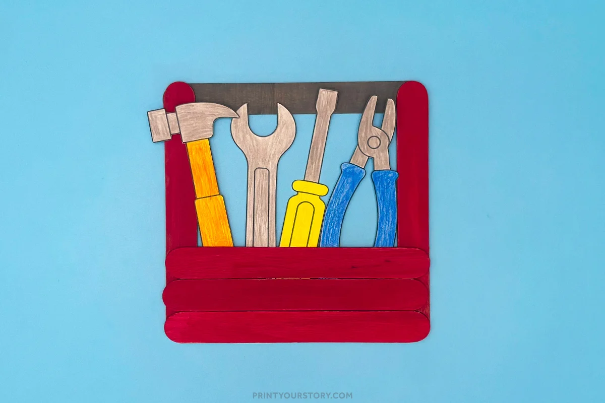 Red popsicle stick toolbox craft holding paper hammer, wrench, screwdriver, and pliers