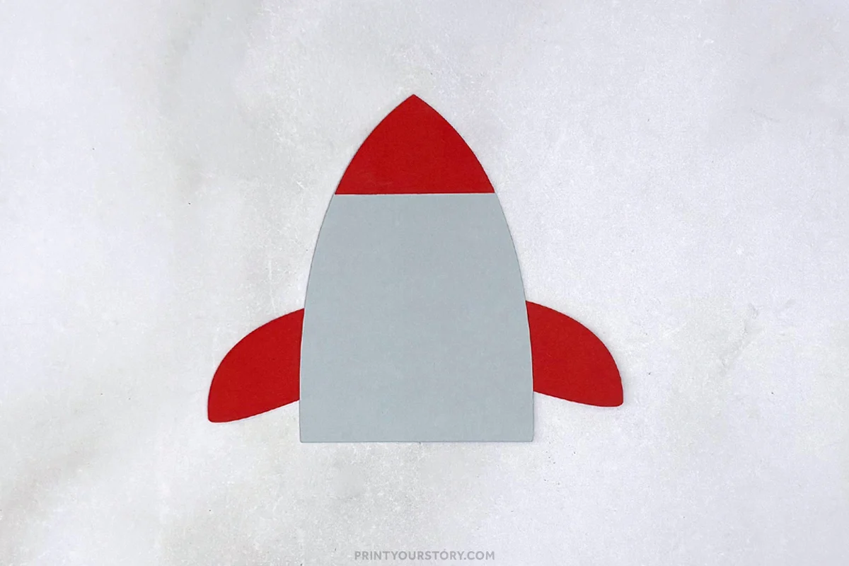 Paper rocket craft with gray body, red nose cone, and red fins on a white background