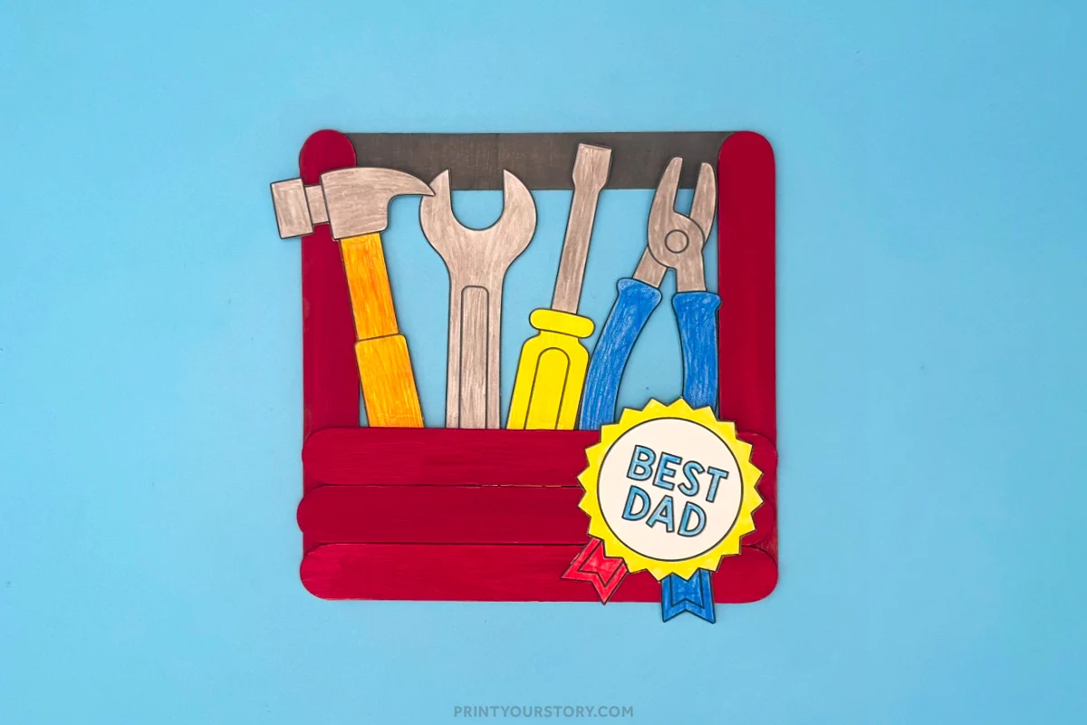 Popsicle stick toolbox craft with paper tools and a “Best Dad” badge on a blue background