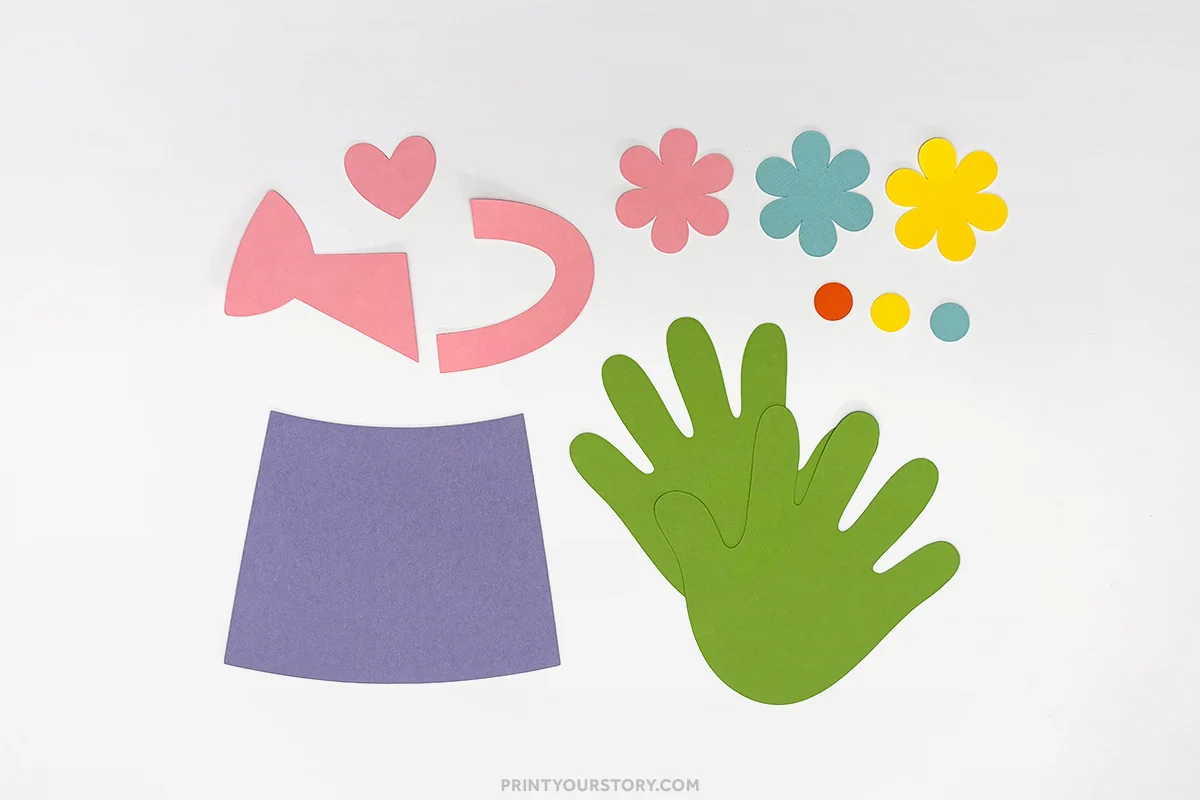 Paper cutouts for a handprint watering can craft, including green handprints, flowers, and watering can pieces