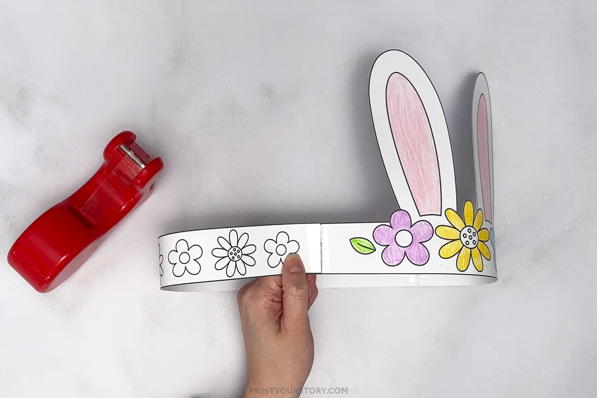 Hand holding a printable bunny headband with paper ears and flowers, with a red stapler nearby