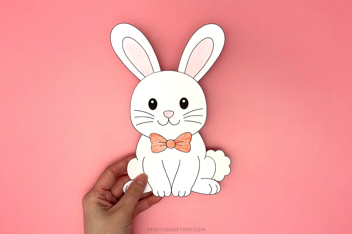Completed printable bunny craft with long ears and orange bow tie held on a pink background