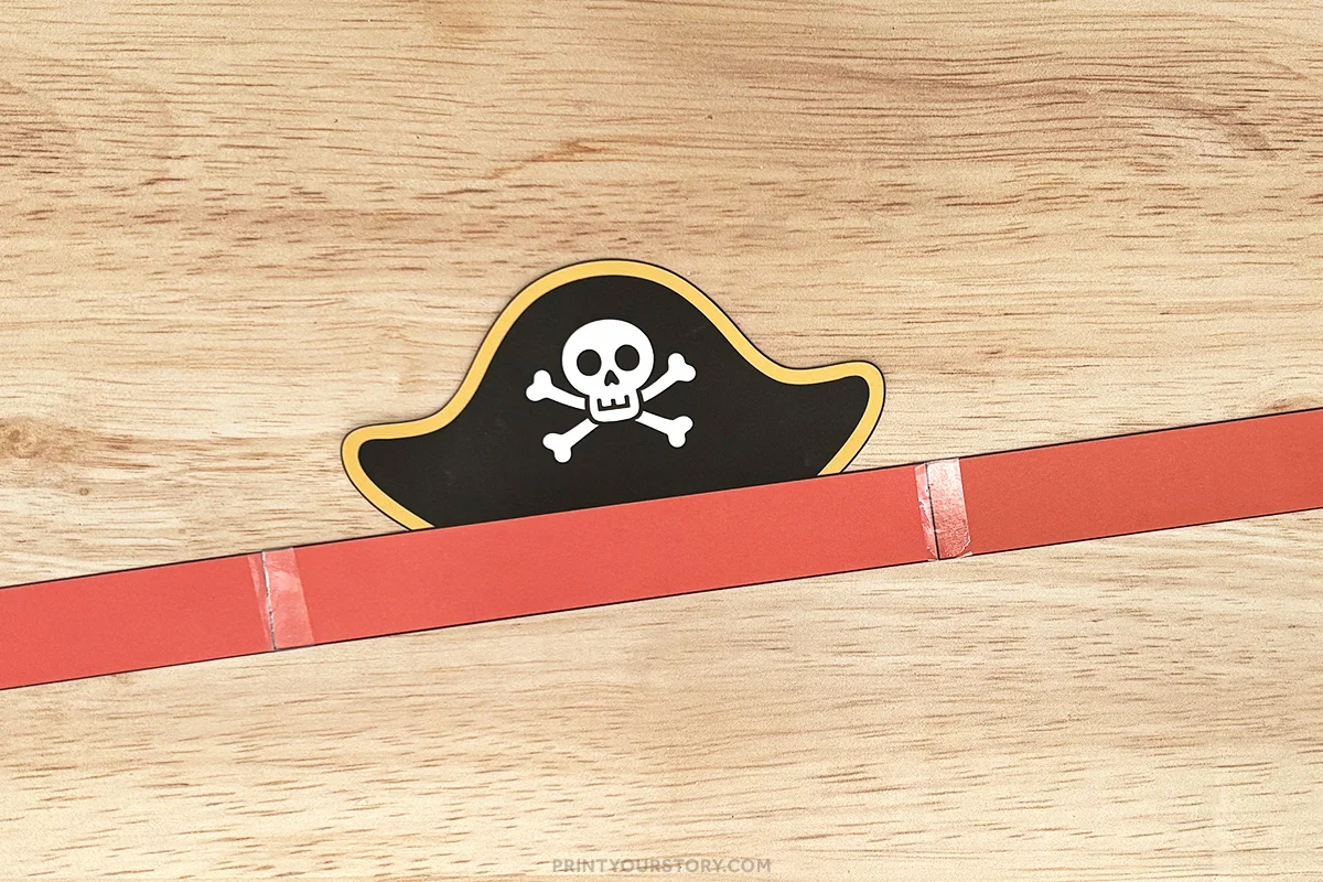 Pirate hat template attached to a red paper headband on a wooden surface
