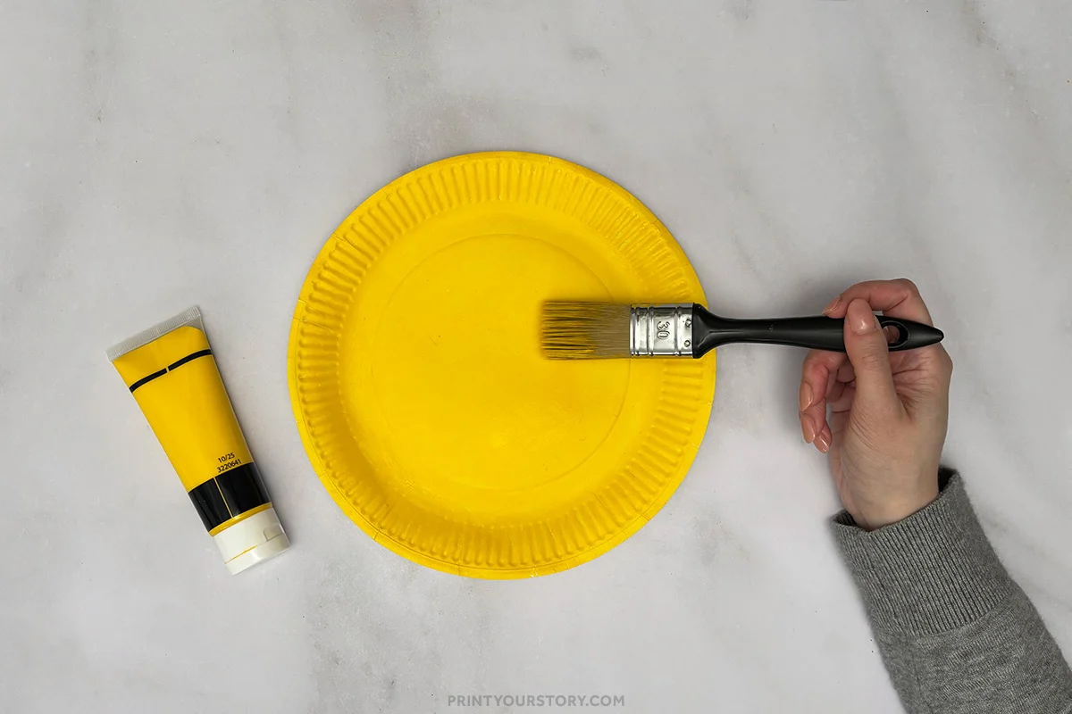 Painting a paper plate yellow with a brush for a giraffe paper plate craft