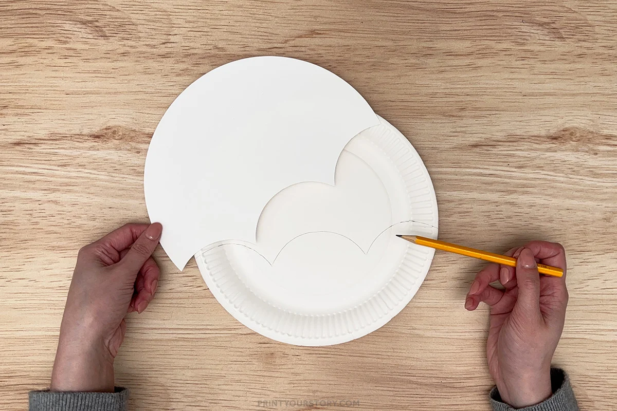 Tracing an umbrella template onto a white paper plate with a pencil