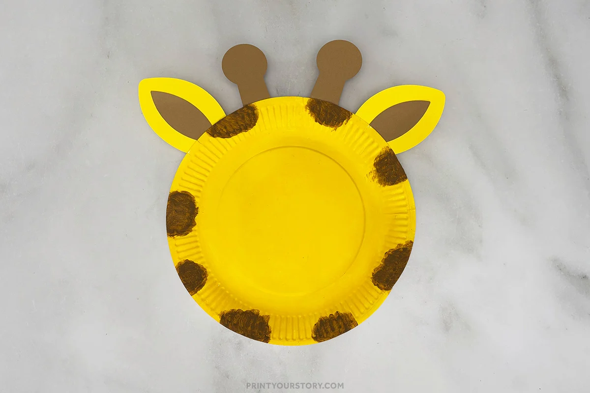 Yellow paper plate giraffe craft with brown spots, ears, and ossicones