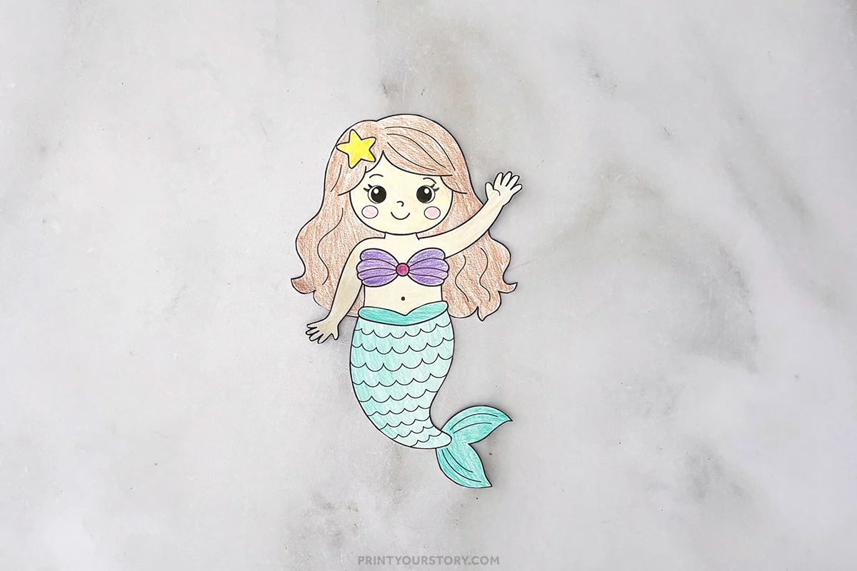 Completed colored paper mermaid craft with peach hair, purple top, and teal tail on a gray surface