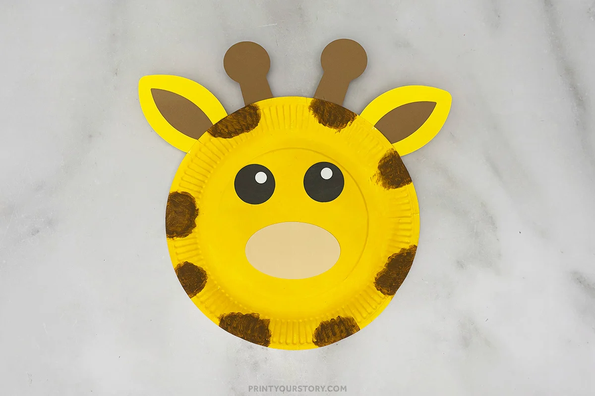 Finished giraffe paper plate craft with ears, ossicones, eyes, muzzle, and brown spots