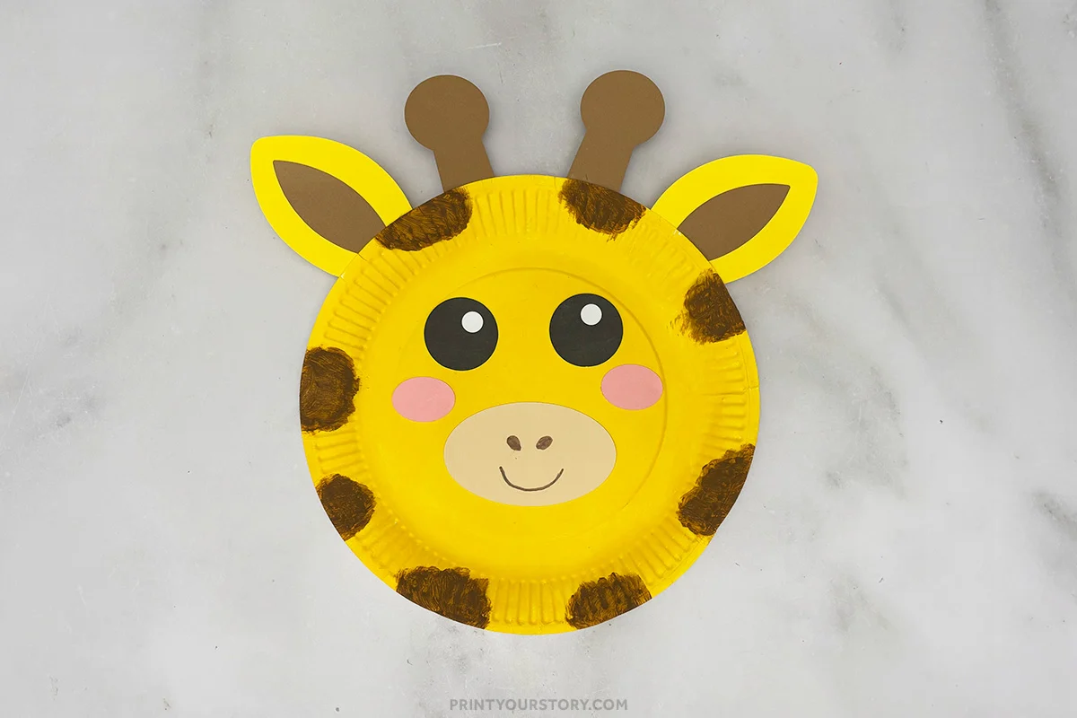 Finished giraffe paper plate craft with ears, horns, spots, and smiling face