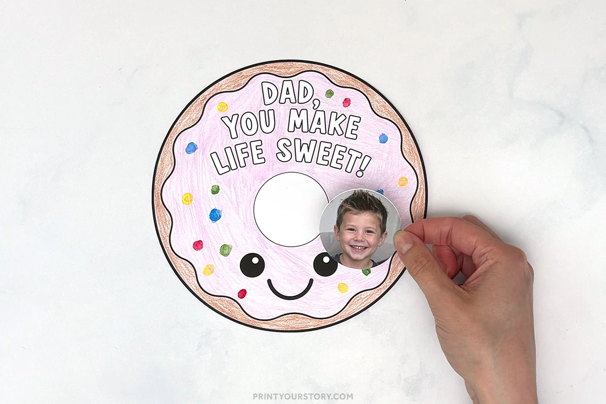 Hand placing a child's photo on a colored donut craft that says, “Dad, you make life sweet!”