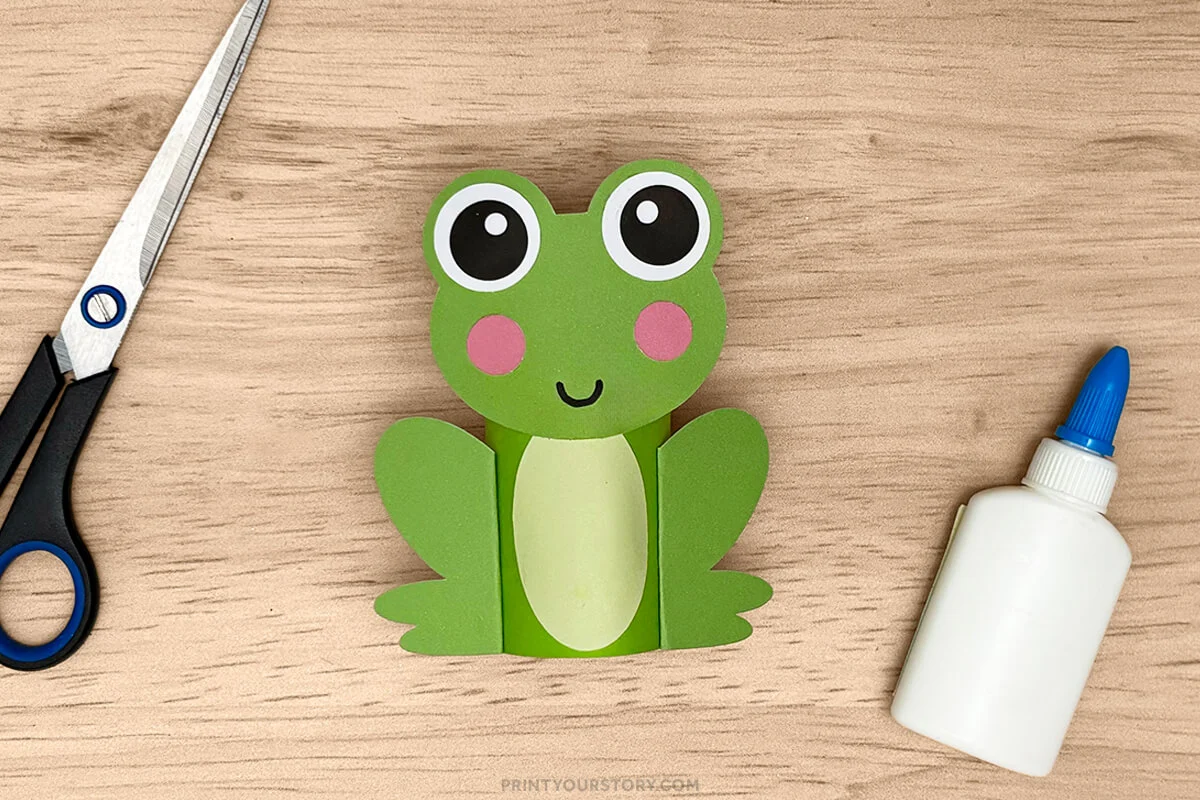 Finished frog toilet paper roll craft with scissors and glue on a wooden table