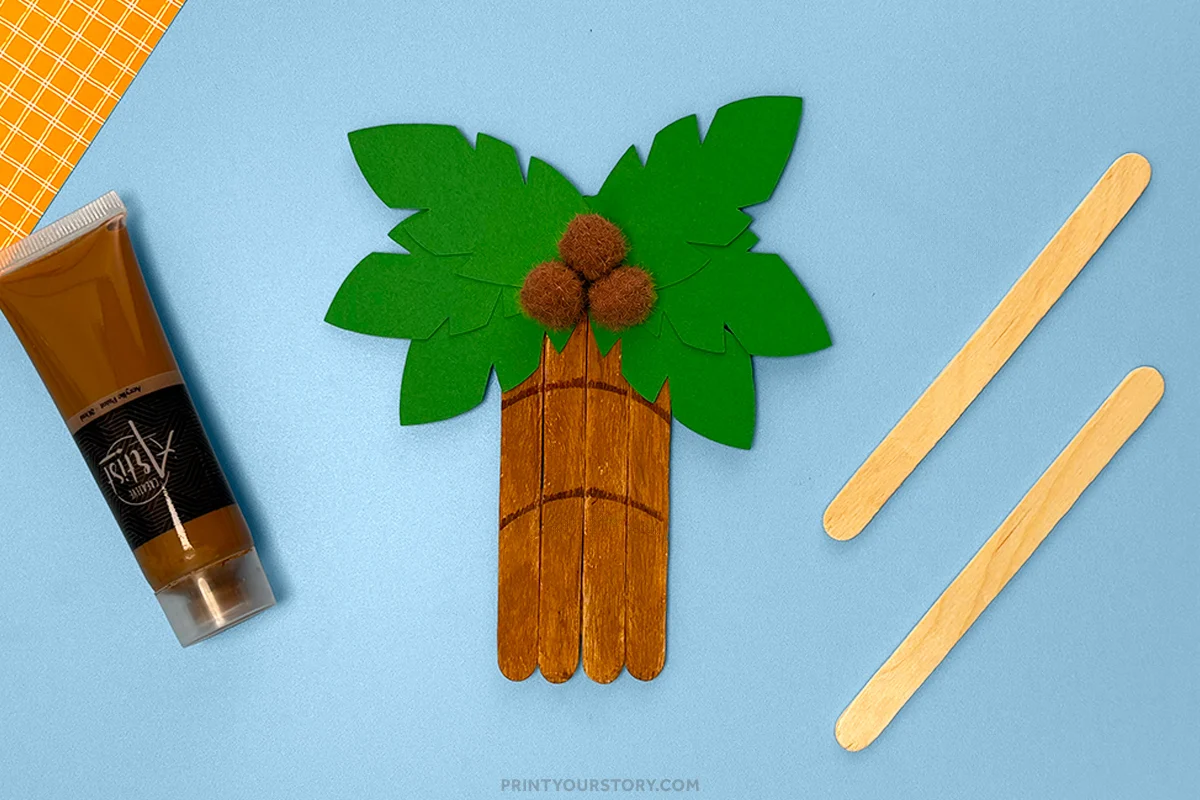 Palm tree popsicle stick craft with green paper leaves and brown pom-pom coconuts