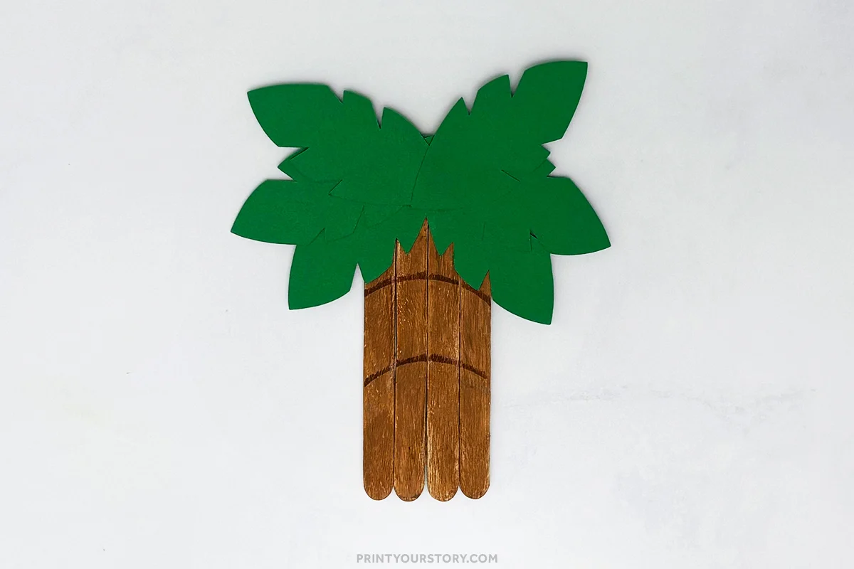 Palm tree popsicle stick craft with brown stick trunk and green paper leaves