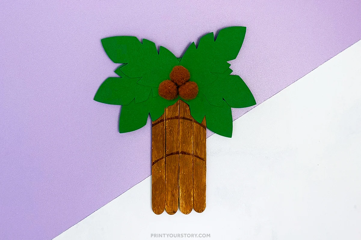 Palm tree popsicle stick craft with green paper leaves and brown pom-pom coconuts