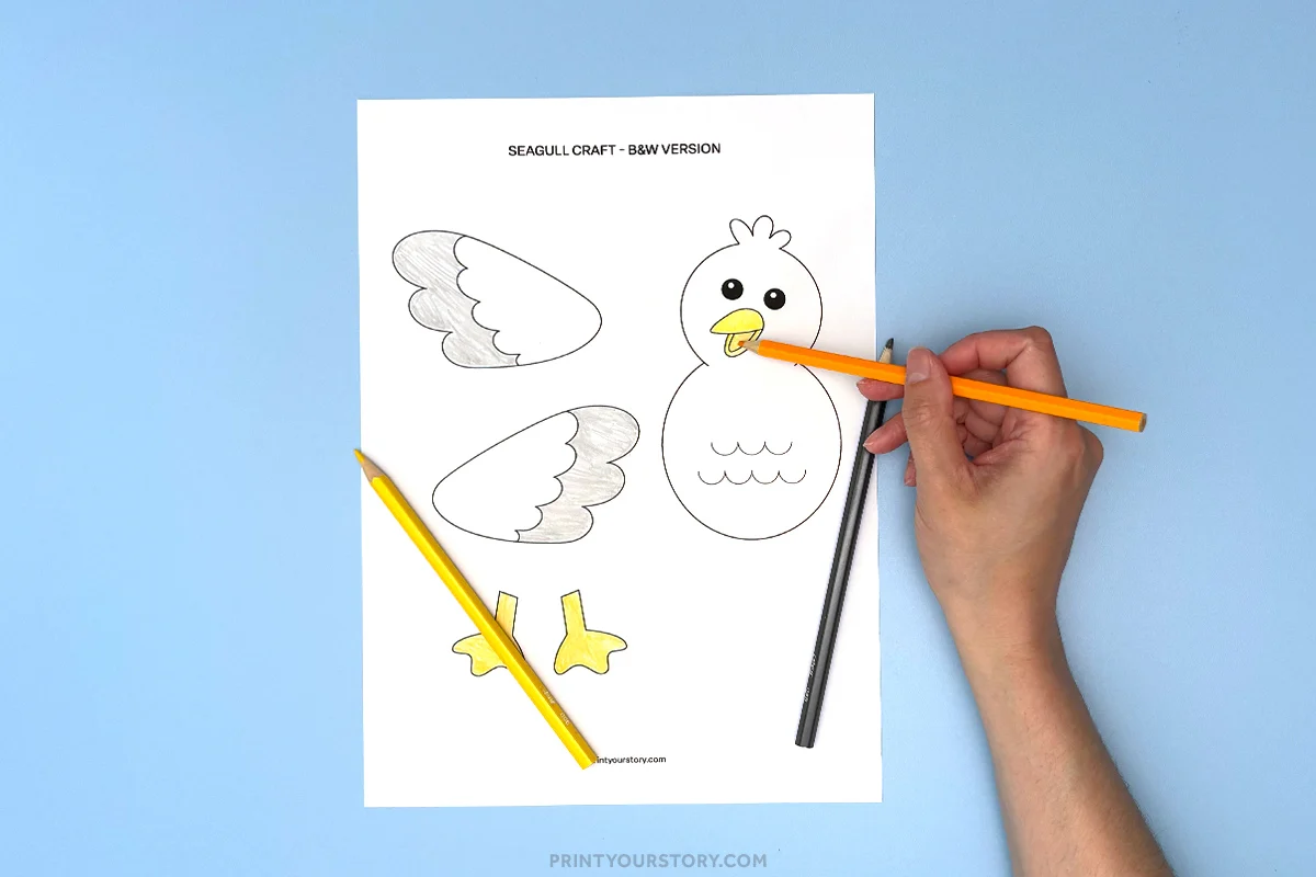 Hand coloring a printable seagull craft template with wings, feet, and body on blue paper